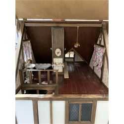 Gerry Welch for Manorcraft Tudor style wooden doll's house, of three-storey multi gabled form with mock beam and plaster walls and simulated leaded glass windows under a felt tiled roof, boarded floors and stairs to each room, curtains to most windows, front entrance door, rear door and single storey extension for kitchen. Furniture includes fitted floral bathroom suite to top floor, well stocked Welsh dresser with copperware etc, tapestry style wall hangings, knole settee, tin bath, metal range, fire-surround, wooden three-piece suite etc; on shaped cobbled base W91cm D61cm H91cm