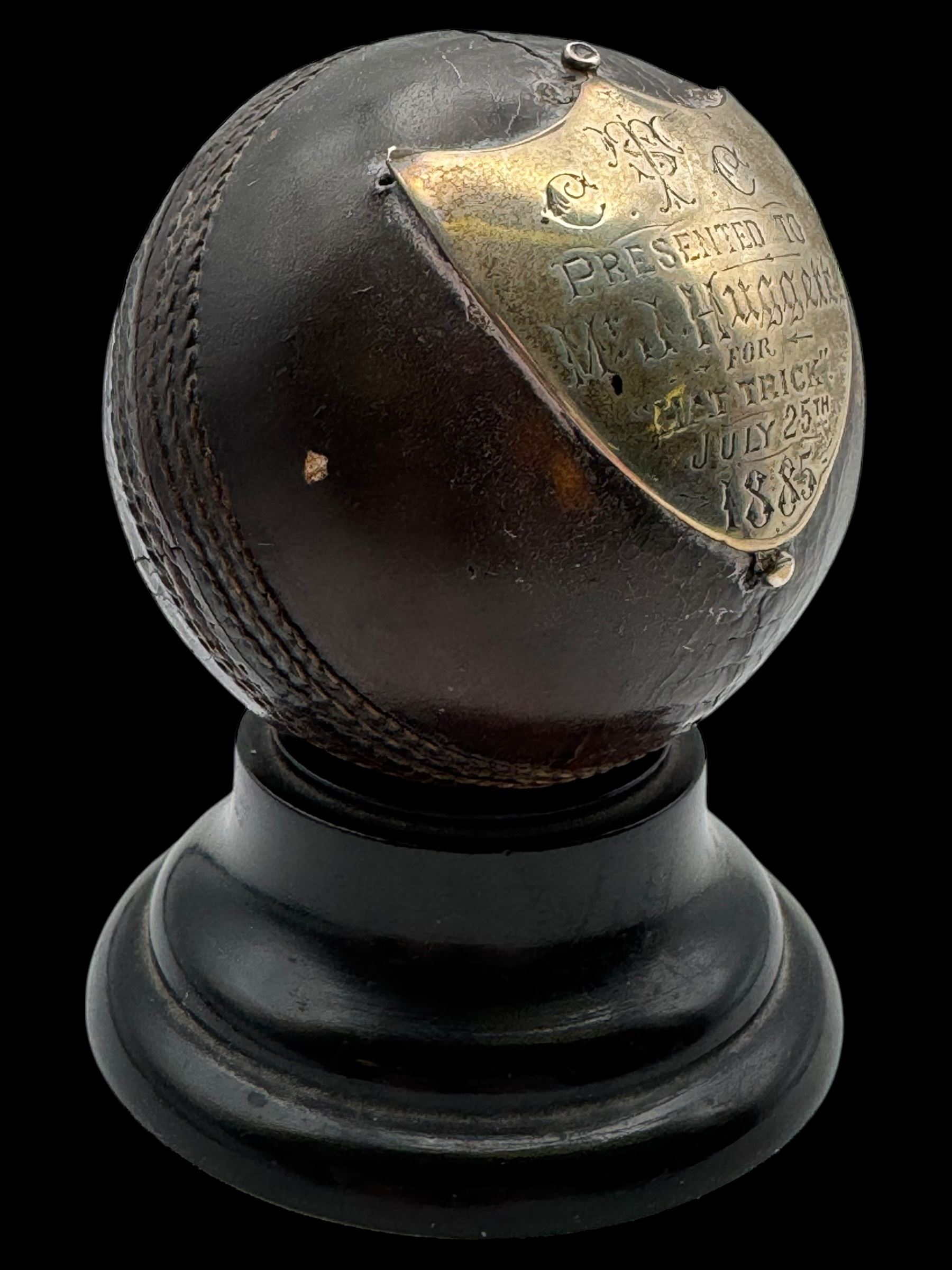 Victorian presentation 'Hat Trick' cricket ball, with applied silver shield cartouche presented to Mr J Hugger 1885, upon ebonised wooden stand