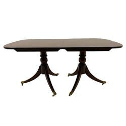 Regency style cross banded mahogany twin pedestal dining table, extending with additional leaf, on twin pillars each with three splayed supports terminating at brass paw cups and castors 