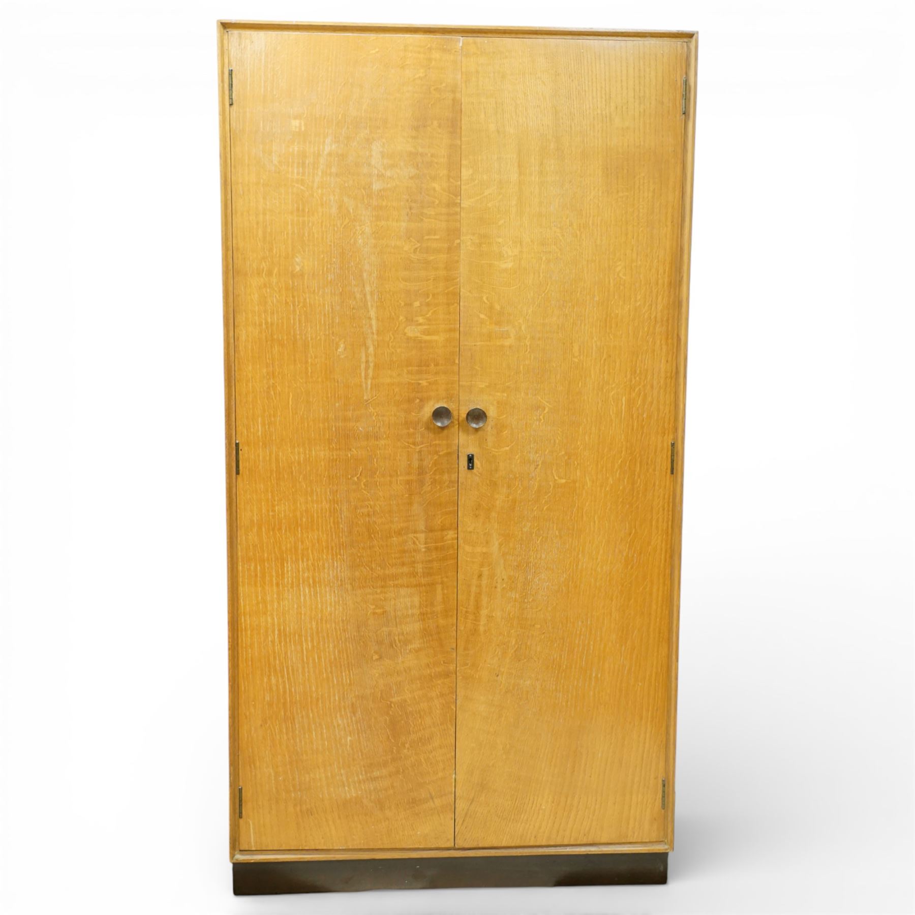 Mid 20th century oak veneered wardrobe, the plain rectangular top above a pair of hinged doors fitted with circular handles, opening to reveal a hanging rail and upper shelf, one door with inset mirror, the whole raised on a plinth base