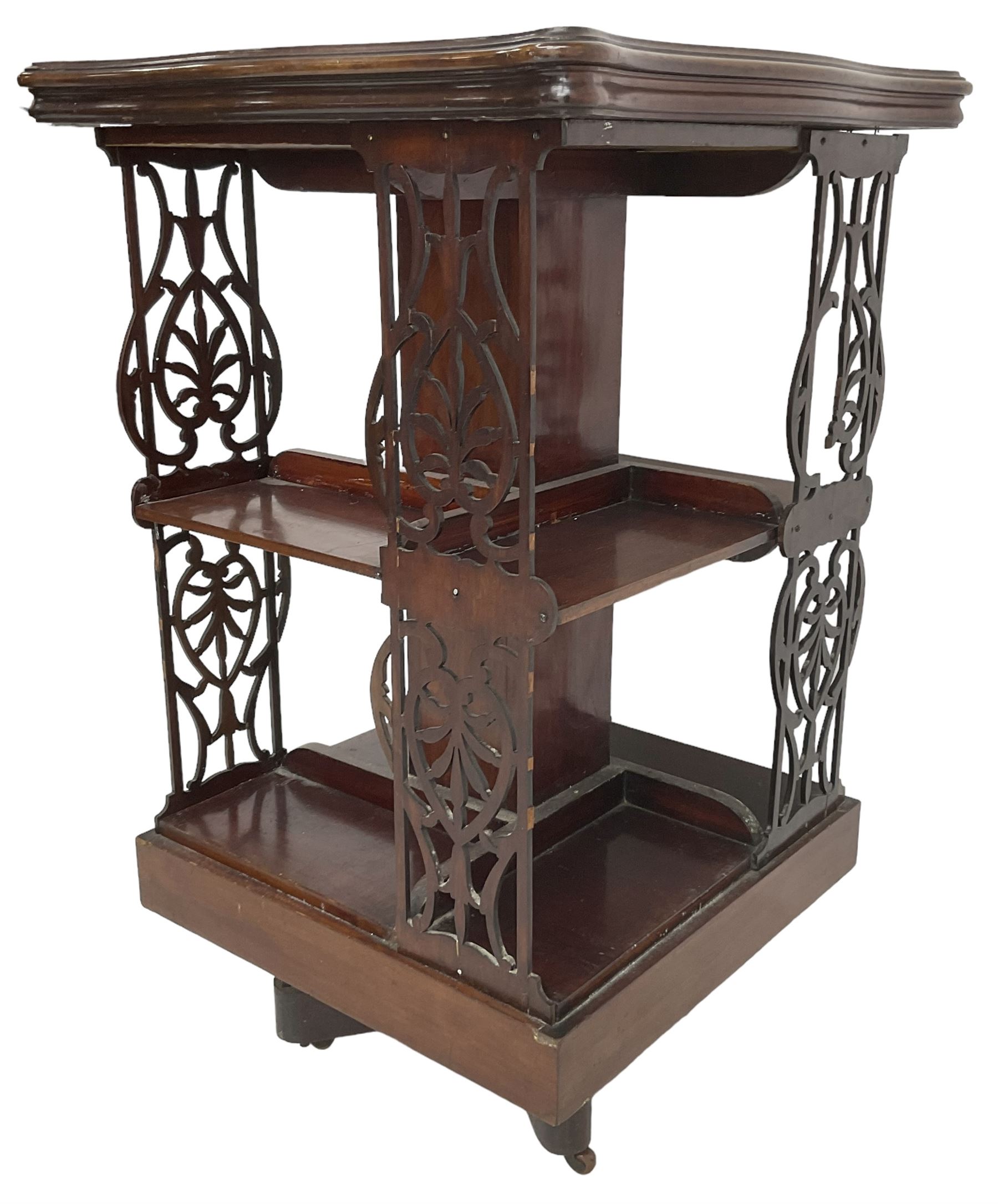 Edwardian mahogany revolving bookcase, the shaped moulded top inlaid with cusped panel and trailing bellflowers within a satinwood frame, foliate pierced upright splats and central square column supporting two tiers, on cruciform base with brass and ceramic castors 
