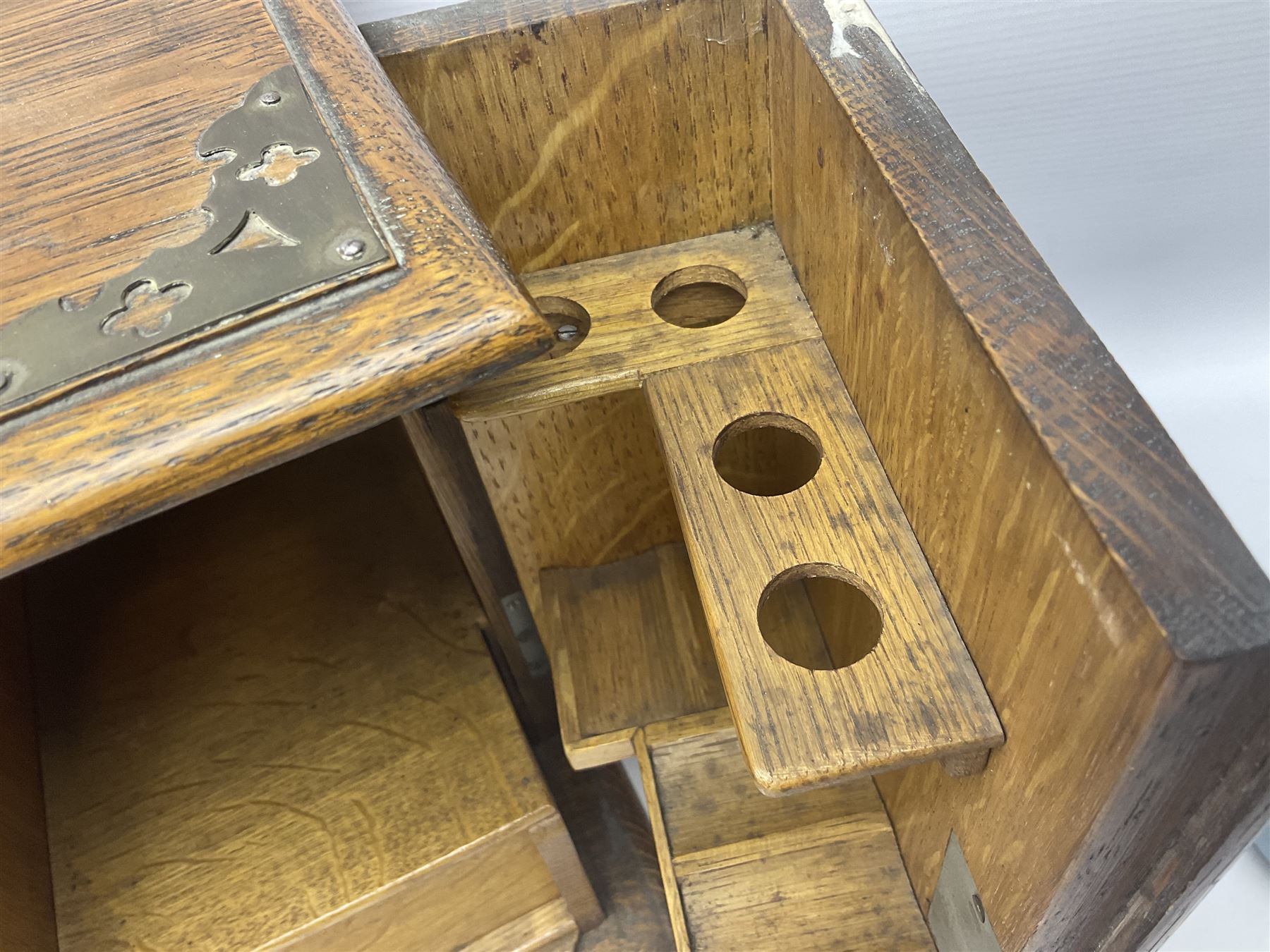 Early 20th century oak smokers cabinet, with brass shield shaped mounts, opening to reveal a compartmentalised interior with three drawers, pipe rack and tobacco jar, together with a small wooden shelf, smokers cabinet H28.5cm