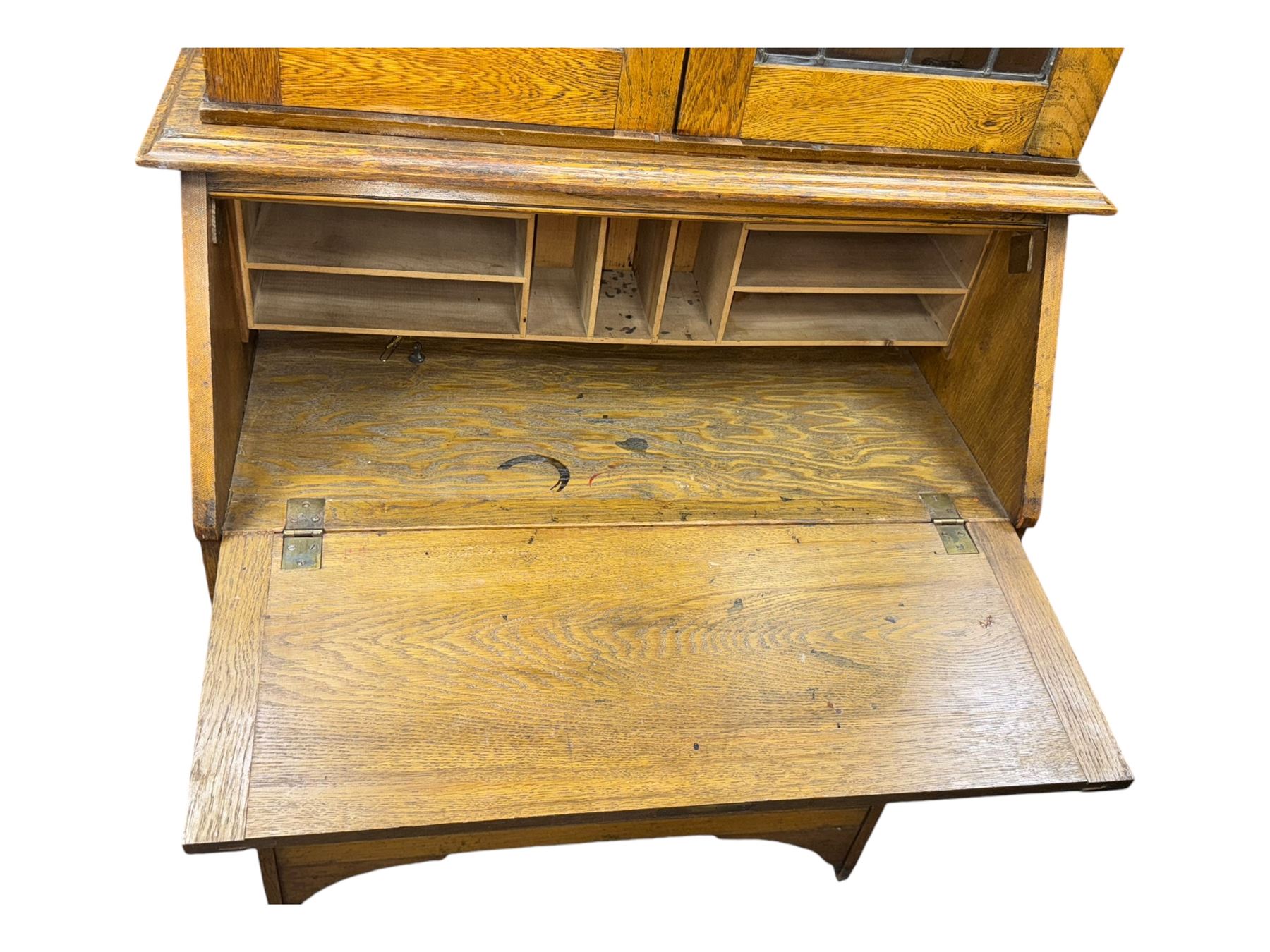 Early 20th century Arts and Crafts oak bureau bookcase, twin leaded and glazed stained glass doors enclosing two shelves, over bureau section with fall-front inlaid with sunburst motif, fitted interior of pigeonholes and shelves, on bracket feet