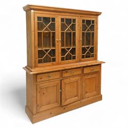 Mid 20th century pine glazed dresser on cupboard base, upper section of rectangular form with three astragal glazed hinged doors enclosing two adjustable wooden shelves and projecting frieze over three short drawers and three hinged panelled cupboard doors with brass handles, the front and sides, raised on a plinth base 