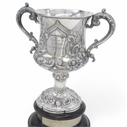 Victorian silver twin handled trophy, the bowl embossed with floral and scrolling decoration, with presentation engraving to body and twin acanthus capped C scroll handles, upon a lobed foot, hallmarked London 1866, maker's mark AM probably for Alexander Macrae, upon an ebonised wooden plinth, trophy only H25.5cm