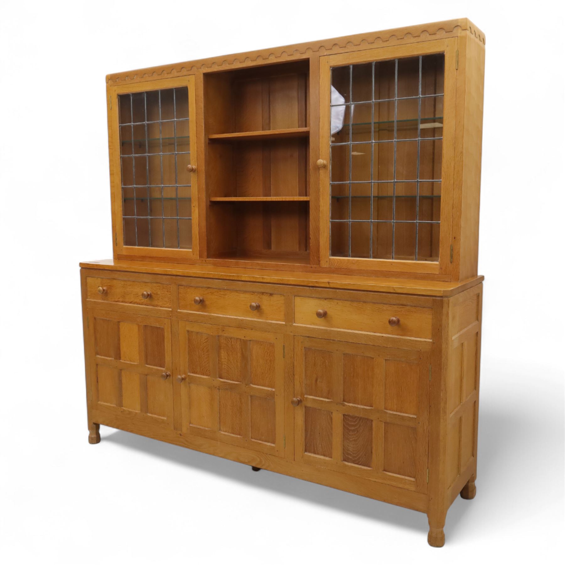 David 'Oakleafman' Langstaff - oak three drawer dresser, the scalloped cornice above a back with central open shelves flanked by two glazed and leaded cupboard doors opening to glass shelves, upon a base with adzed top carved with signature leaf, three drawers and three panelled cupboard doors with turned handles, upon octagonal feet, from the workshop of David Langstaff, Easingwold, Yorkshire
