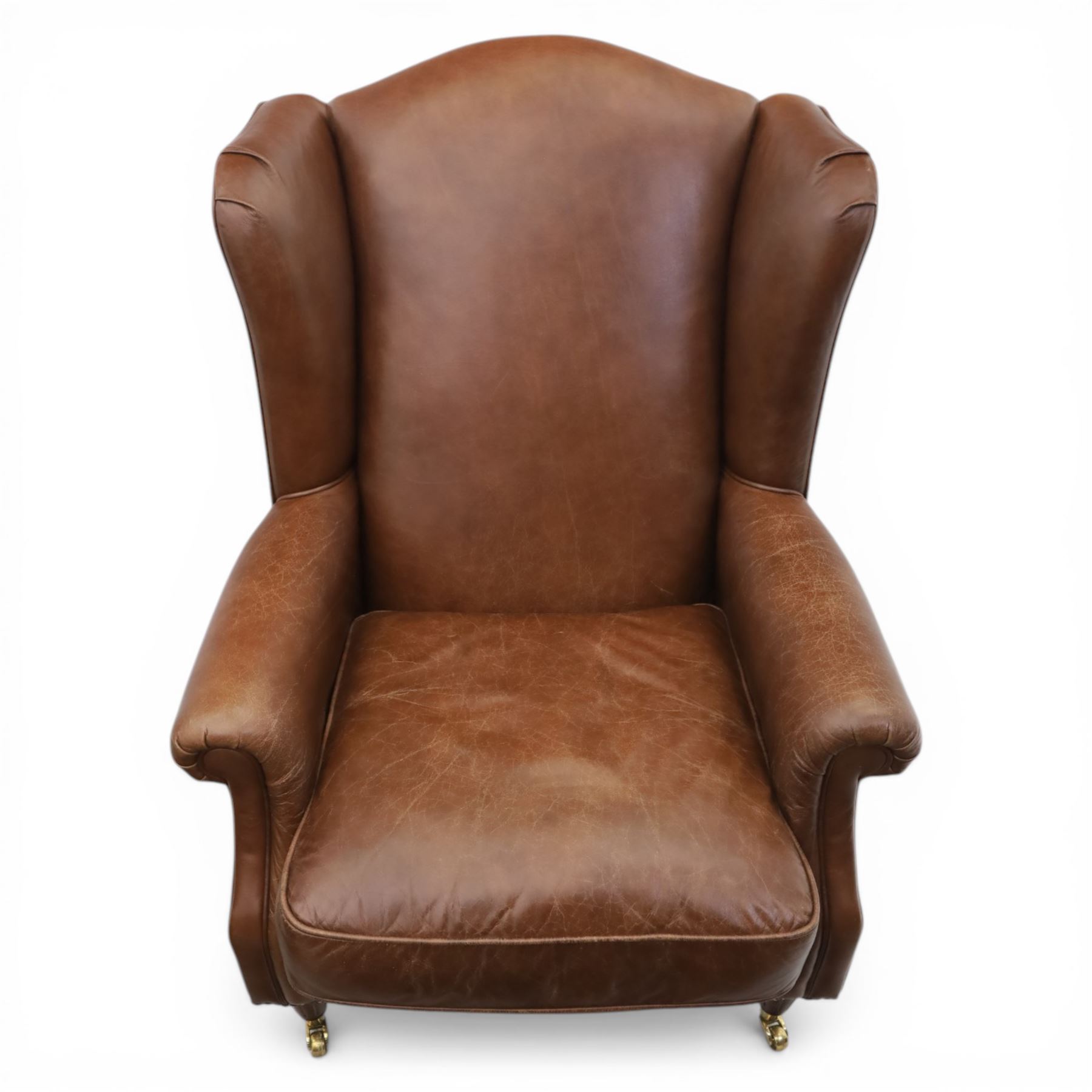 Laura Ashley - Pair of brown leather wingback armchairs, with scrolled arms and loose cushion seat, brass studded trim, on cylindrical tapering legs terminating in castors