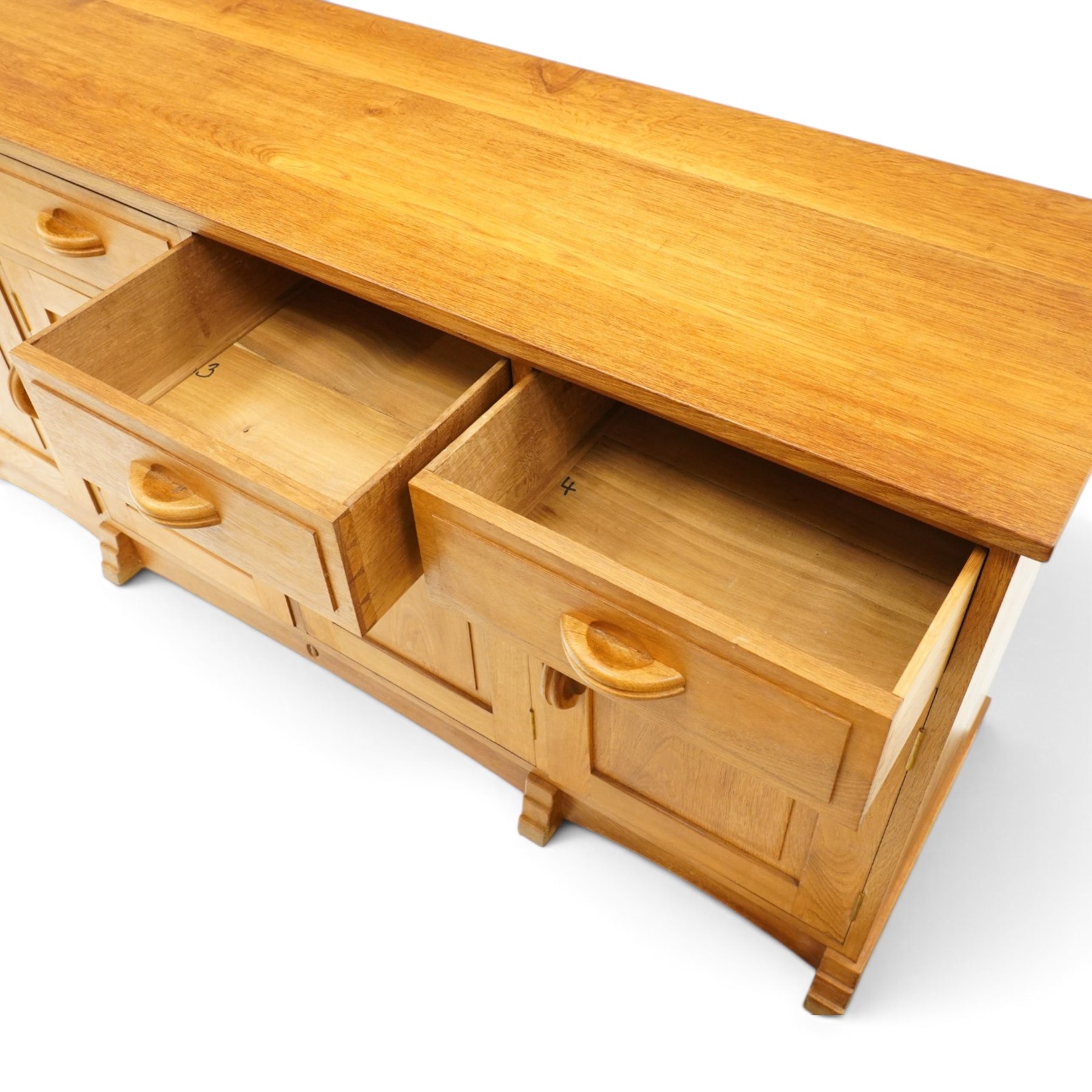 Acorn Industries - oak dresser base or sideboard, the rectangular top over three drawers with protruding oak handles, over four panelled cupboard doors enclosing a single shelf, raised on stepped feet, carved with acorn signature, by Alan Grainger, Brandsby