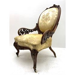 Victorian walnut lady’s drawing room chair, the cameo back cresting rail carved with scrolled foliate and central cartouche, scrolled open arms pierced and carved with flowers, upholstered in gold floral pattern fabric, serpentine sprung seat, carved cabriole supports with brass and ceramic castors 