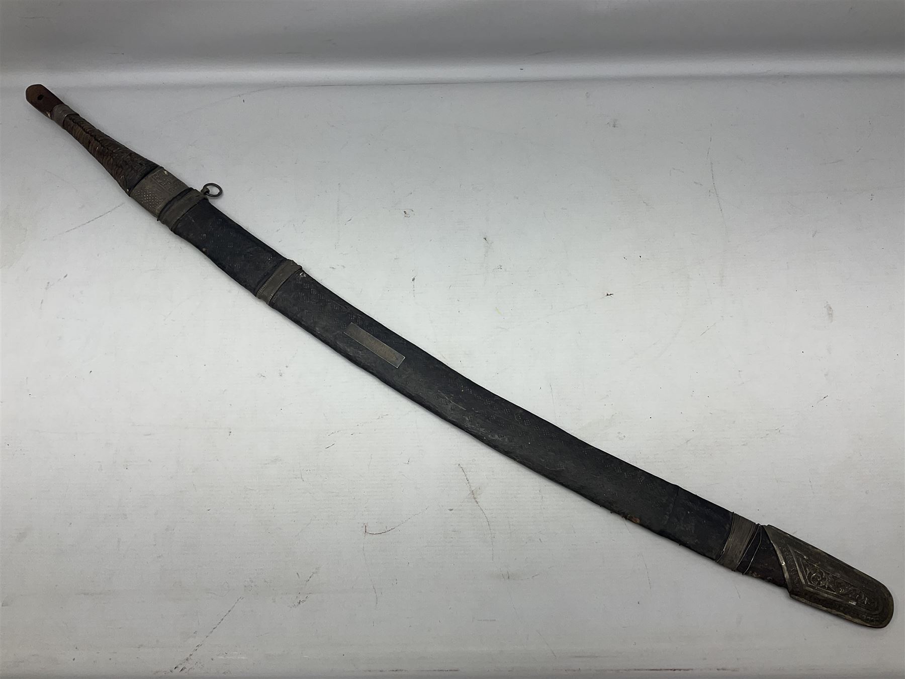 Omani presentation sword kattara, with 77cm  broad slightly curved single edge blade with two fullers, leather bound hilt woven with silver wire decoration and iron pommel;  in tooled leather scabbard with chased silver mounts and presentation plaque 'To Capt. D.M. Naylor From C Company NFR Oman Dec 1962' (Northern Frontier Regiment) L99cm overall