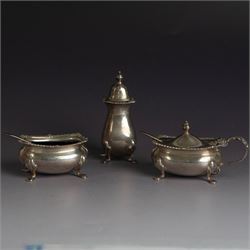 Mid 20th century silver three piece cruet set, comprising pepper shaker, open salt, mustard pot with cover and two condiment spoons, all of oval form with oblique gadrooned rims and upon four paw feet, hallmarked Adie Brothers Ltd, Birmingham 1957, with blue glass liners