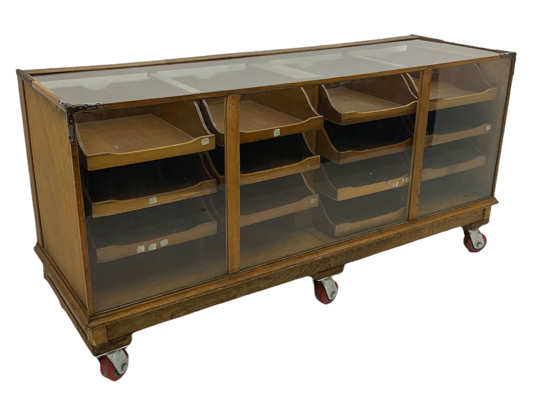 Early 20th century oak framed and glazed haberdashery / shop display cabinet, fitted with sixteen drawers (three missing), on later casters