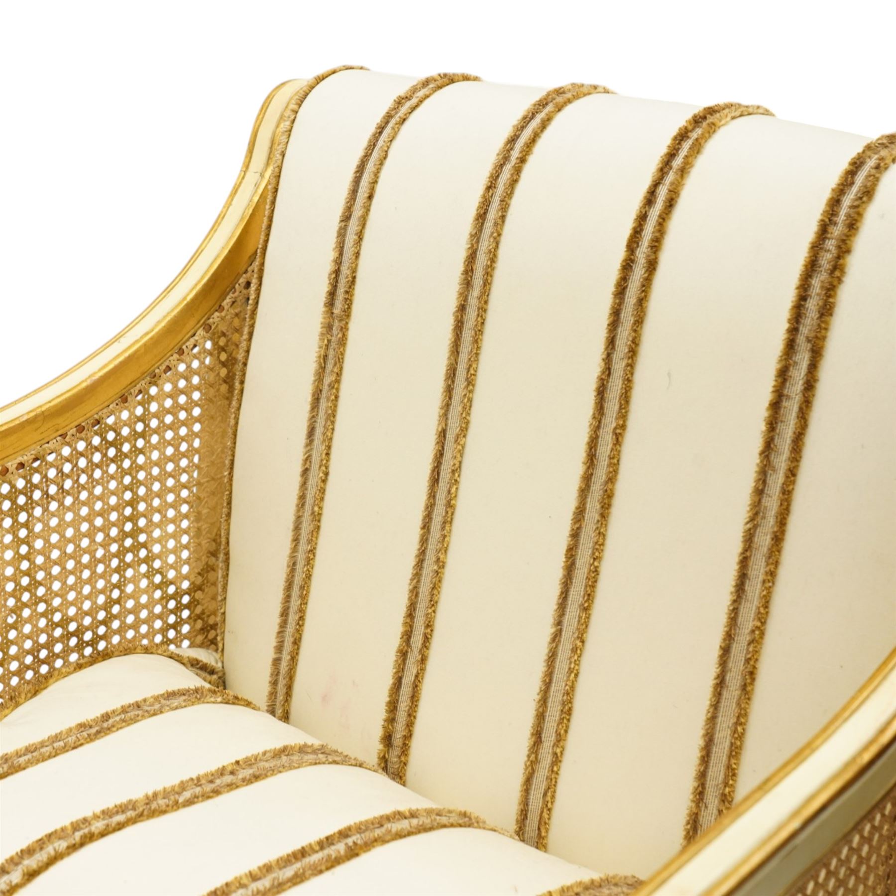 Louis XV design cream painted and parcel-gilt bergere armchair of large proportions, high scrolled back over canework arms, upholstered in striped fabric with over-stuffed loose seat cushion, on fluted supports