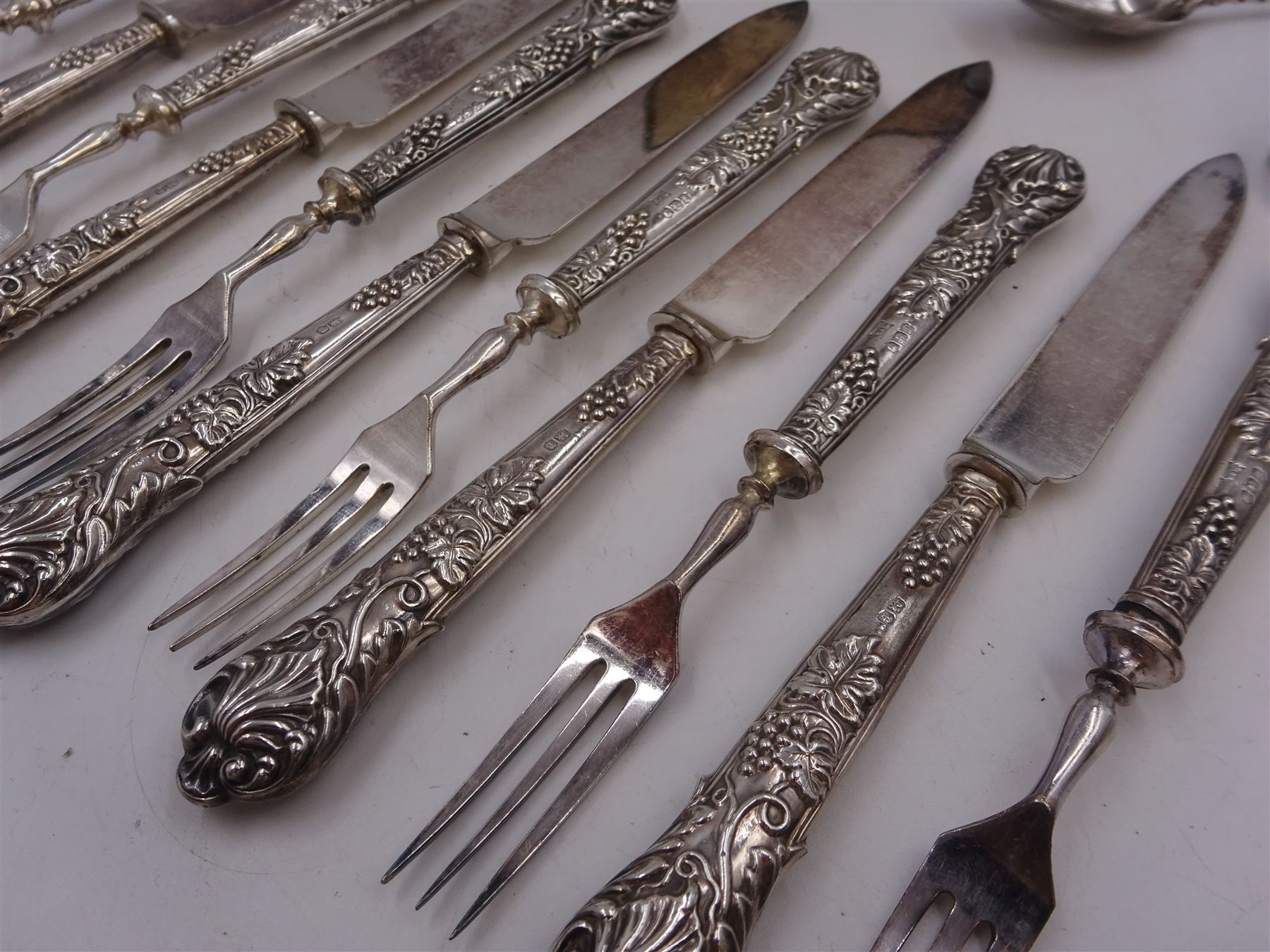 Set of 1930s silver handled fruit knives and forks, for six place settings, the handles decorated in relief with fruiting vines, hallmarked Walker & Hall, Sheffield 1934, together with a set of six 1920s silver egg spoons, with pin prick engraving to handle, hallmarked Thomas Bradbury & Sons Ltd, Sheffield 1929, in fitted case, three silver napkin rings, to include a pair, of octagonal form, with floral engraving, hallmarked John Rose, Birmingham 1951 and two silver souvenir spoons