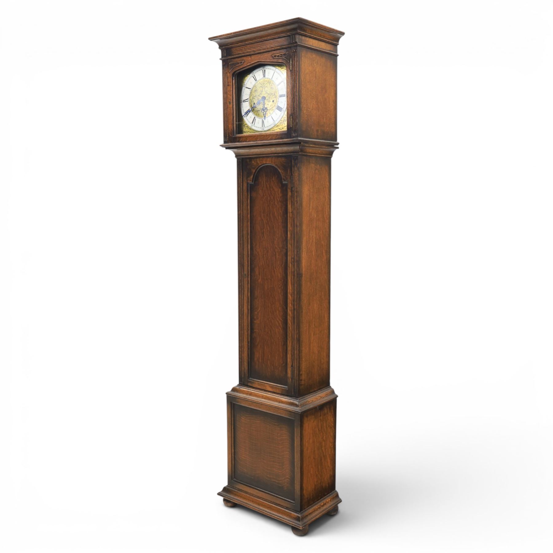 Early 20th century oak longcase clock, square brass dial with engraved foliate spandrels and centre, silvered Roman chapter ring with Arabic minute track, Westminster chime movement, the plain case with glazed arched trunk door and moulded plinth