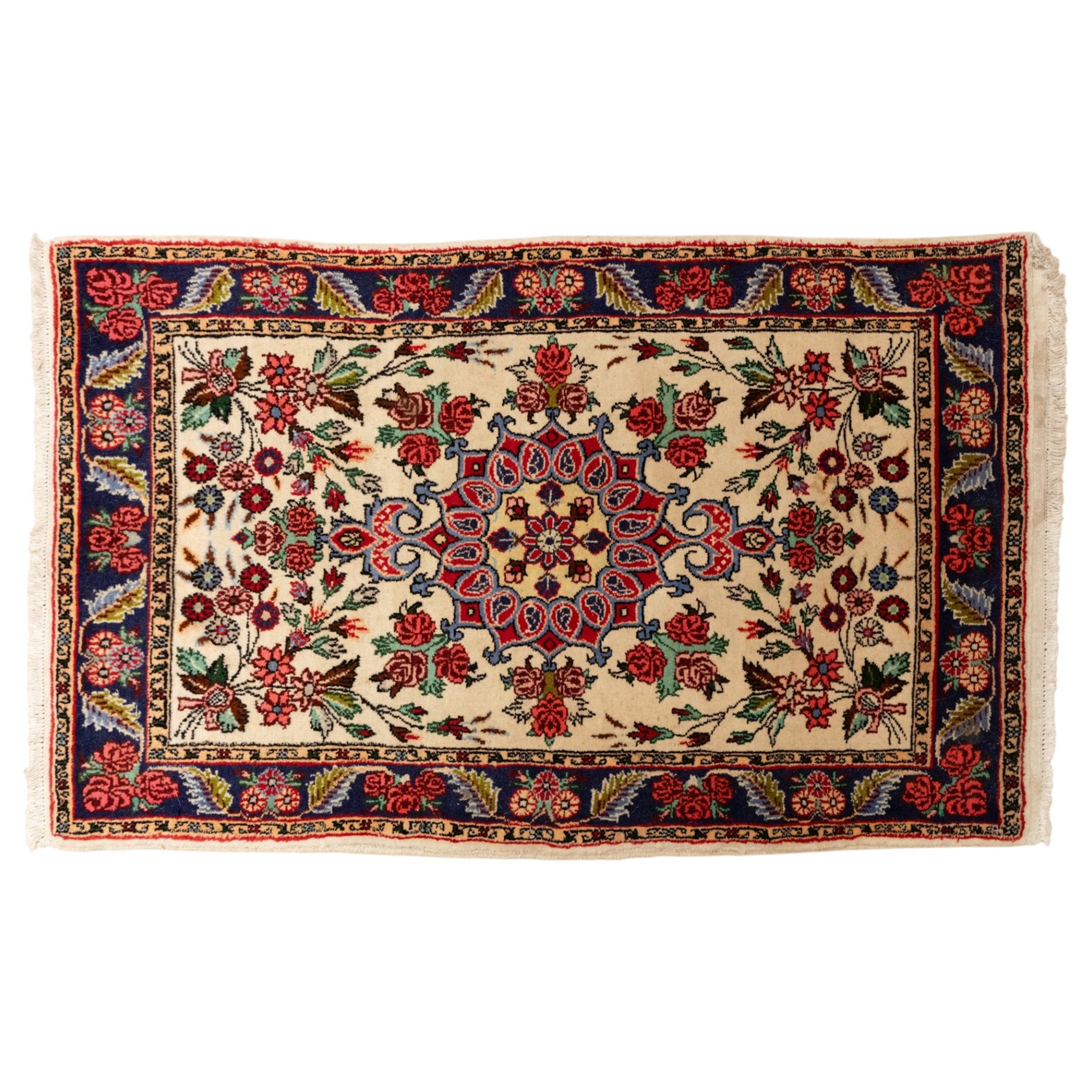 Two small rugs, an ivory ground example decorated with a central floral medallion and scattered rose sprays, enclosed by a navy foliate border (62cm x 101cm), and a crimson pictorial mat worked with seated figures, an animal and birds amongst flowering plants (45cm x 79cm) (2)