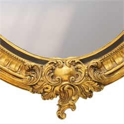 Pair of Rococo Revival gilt framed oval wall mirrors, the exuberant pediment formed of scrolling acanthus leaves and rocaille ornament, the oval bevelled plate set within with ebonised slip with outer repeating lappet decoration, over a rocaille cartouche terminal