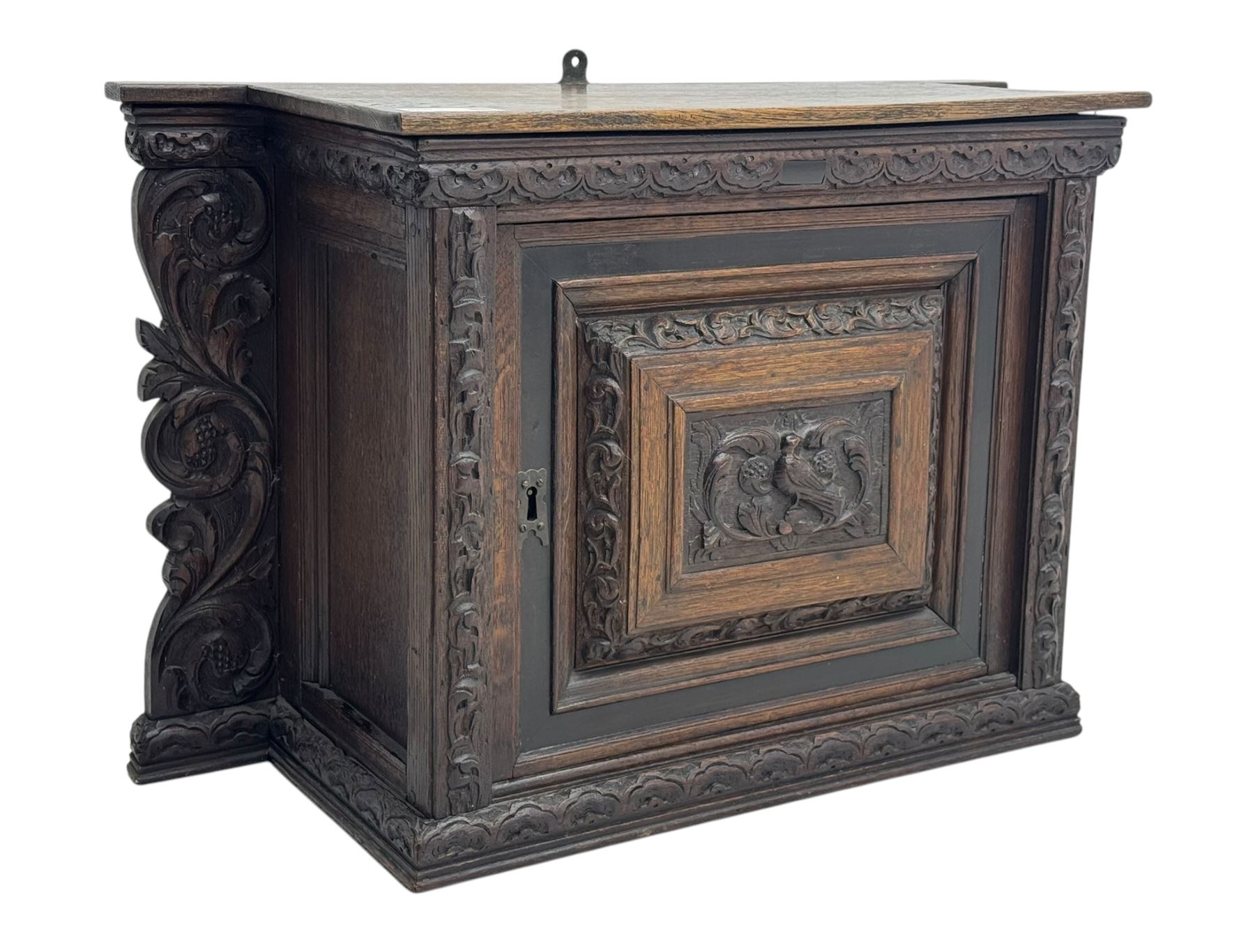 18th century and later carved oak cupboard, enclosed by panelled door carved with central bird motif and scrolled leafage with an outer ebony band, the frieze and uprights carved with repeating lunette and floral designs, flanked by scrolled foliate carved upright brackets