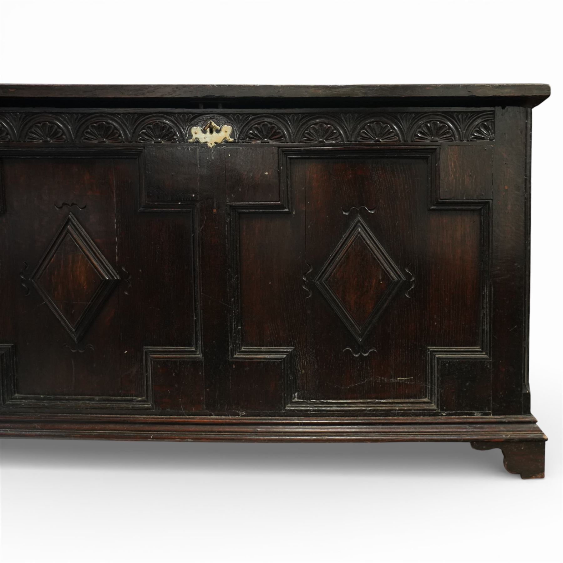 18th century oak coffer, the three panel hinged lid above a frieze carved with repeated lunettes, the front formed with geometric moulded panels centred by lozenge motifs, raised on bracket feet