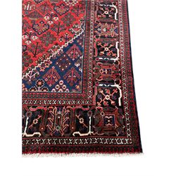 Persian Joshaghan crimson ground rug, stepped lozenge medallion surrounded by repeating foliate lozenge motifs, the border decorated with stylised plant motifs, within geometric guard stripes