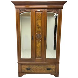 Edwardian walnut double wardrobe, enclosed by two bevelled mirror doors flanking central figured panel with foliate carved decoration, fitted with single drawer to base