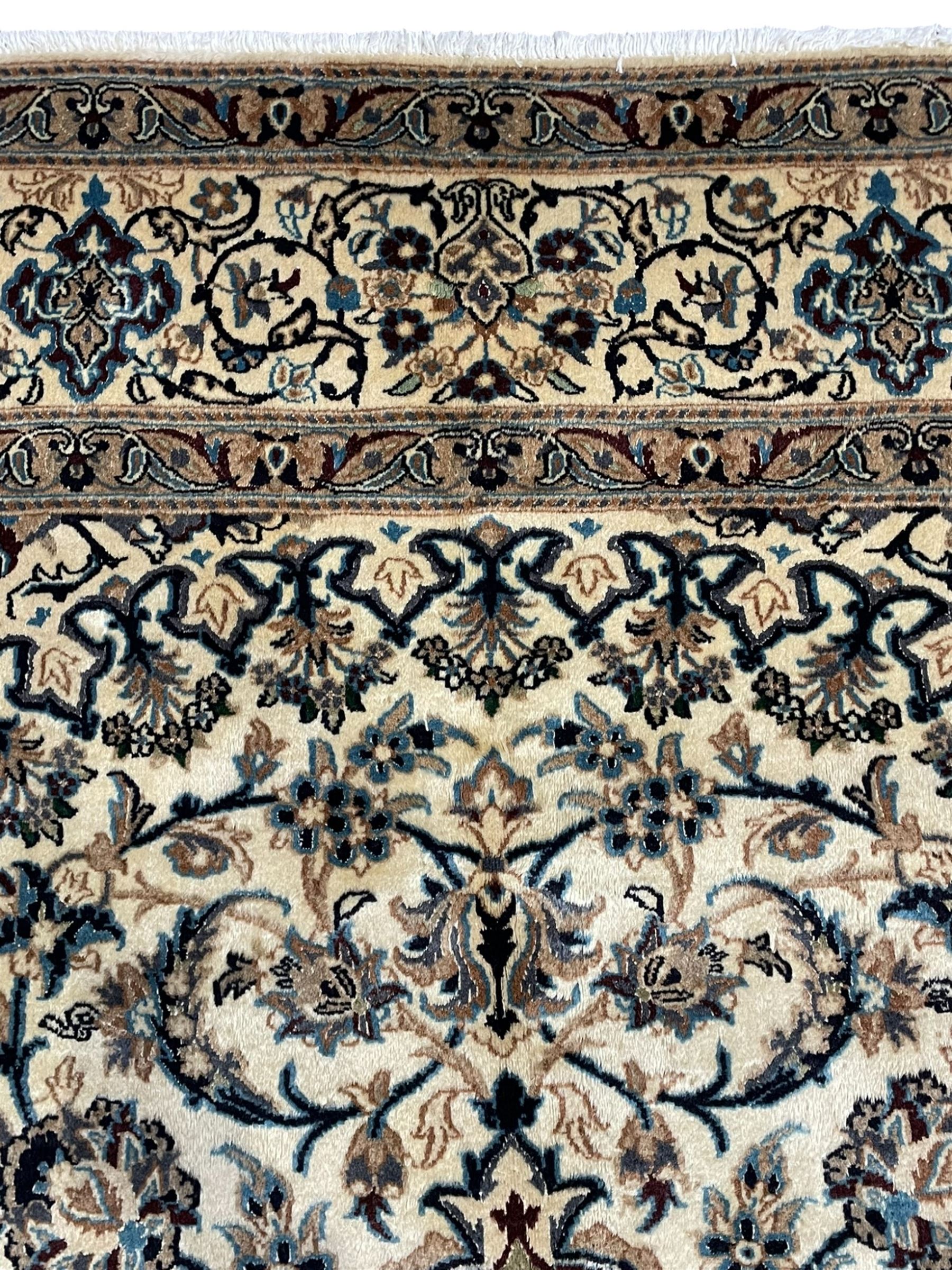 Persian Kashan ivory ground carpet, central rosette medallion surrounded by swirling leafy branches and floral sprays, the main border with scrolling pattern interspersed with floral motifs, within guard stripes 