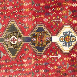 South West Persian hand-knotted Qashgai runner, madder-red field with a central column of linked diamond medallions in tones of indigo, ochre, ivory, and green, surrounded by stylized floral and boteh motifs within a cream border of angular vines and serrated devices, with cotton fringe ends   