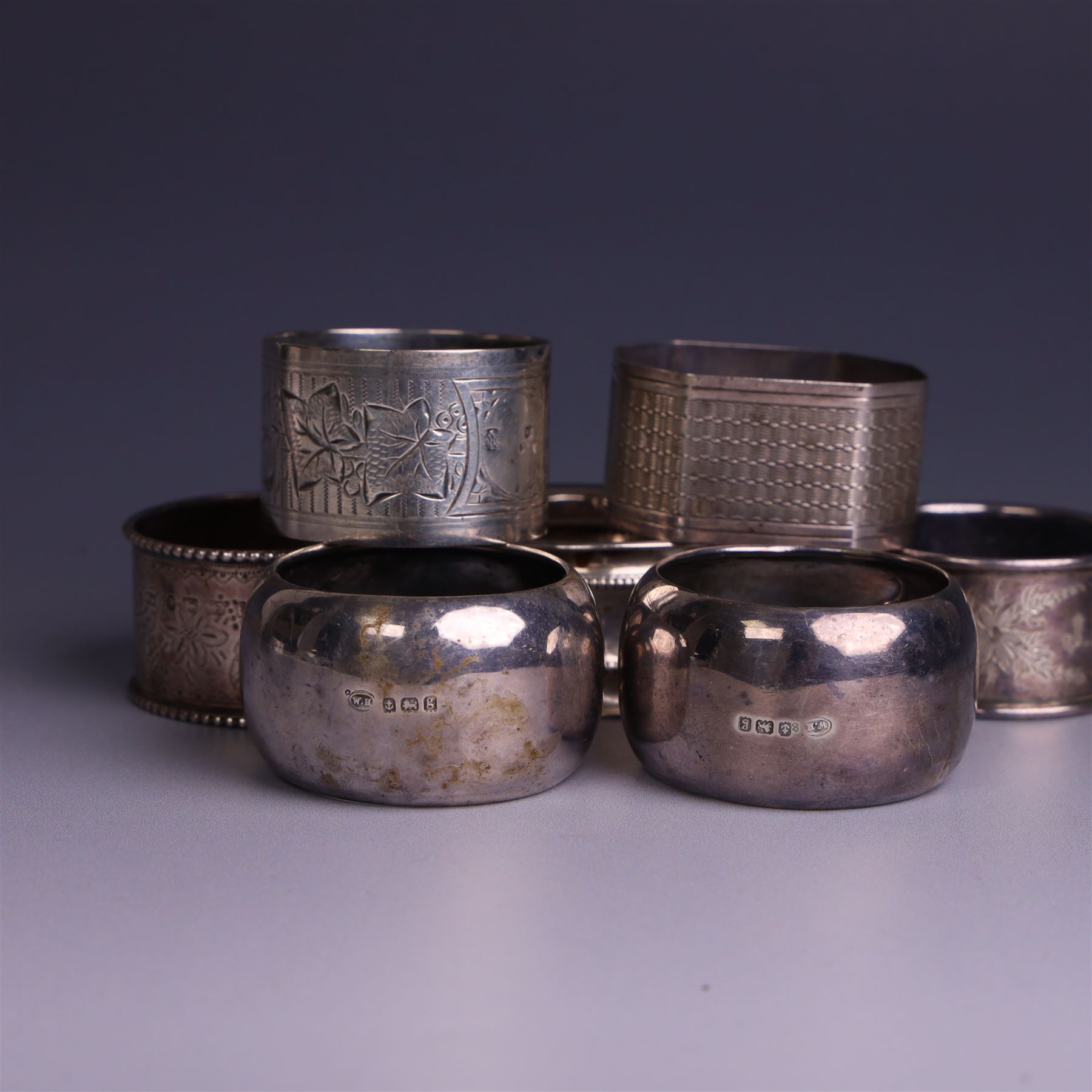 Seven silver napkin rings, of varying design and each with engraved initials, all hallmarked