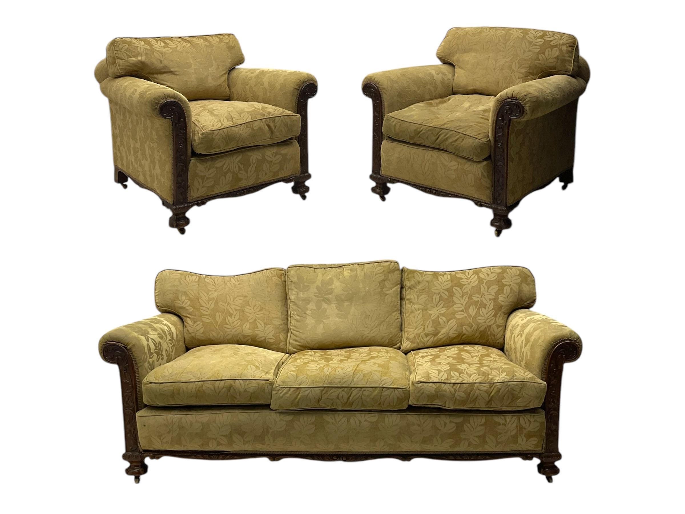 Early 20th century mahogany framed three-piece lounge suite - three-seat camelback sofa (W203cm, D105cm); pair of matching armchairs (W95cm, D96cm); upholstered in neutral foliate pattern fabric, carved with trailing leafy branches, ball and claw carved feet with brass castors 