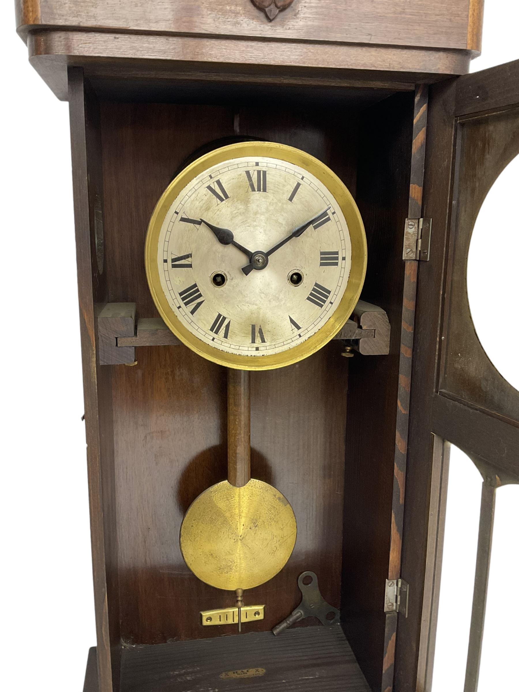 1930s wall clock in an oak case with a crested pediment and glazed door with visible pendulum, silvered dial with Roman numerals and steel spade hands, eight day spring driven movement striking the hours and half hours on a gong. With pendulum and key.