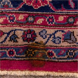 Large Persian-style mahal-type hand-knotted carpet, of rectangular form with a deep crimson field decorated with an all-over arrangement of stylized floral sprays and palmettes, with a central subtle medallion composition enclosed by a dark navy main border of scrolling floral motifs between narrow guard stripes with fringe ends 