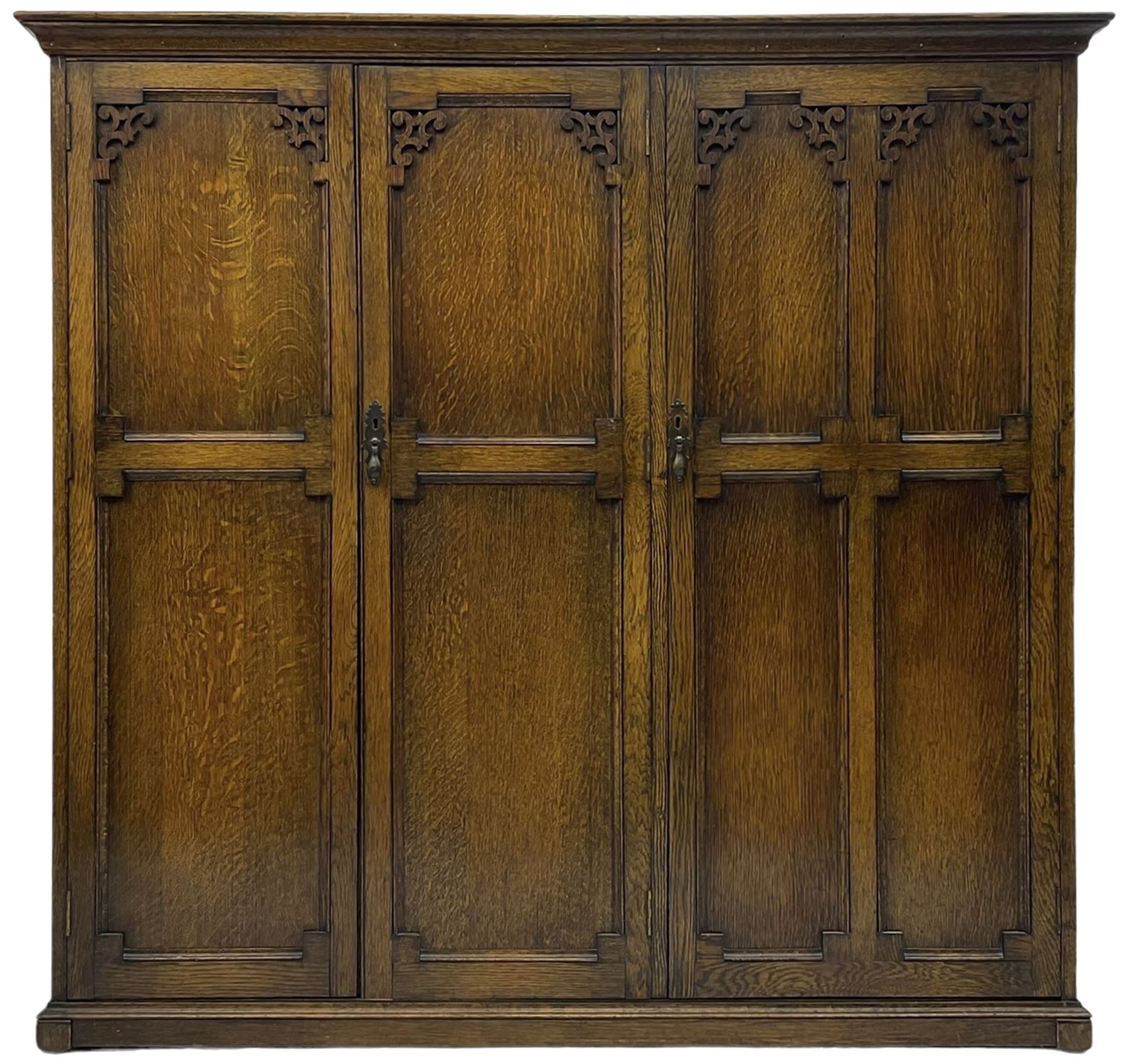 Early 20th century oak triple wardrobe, three panelled doors with geometric mouldings and fretwork spandrels, the interior fitted with slides and hanging rail