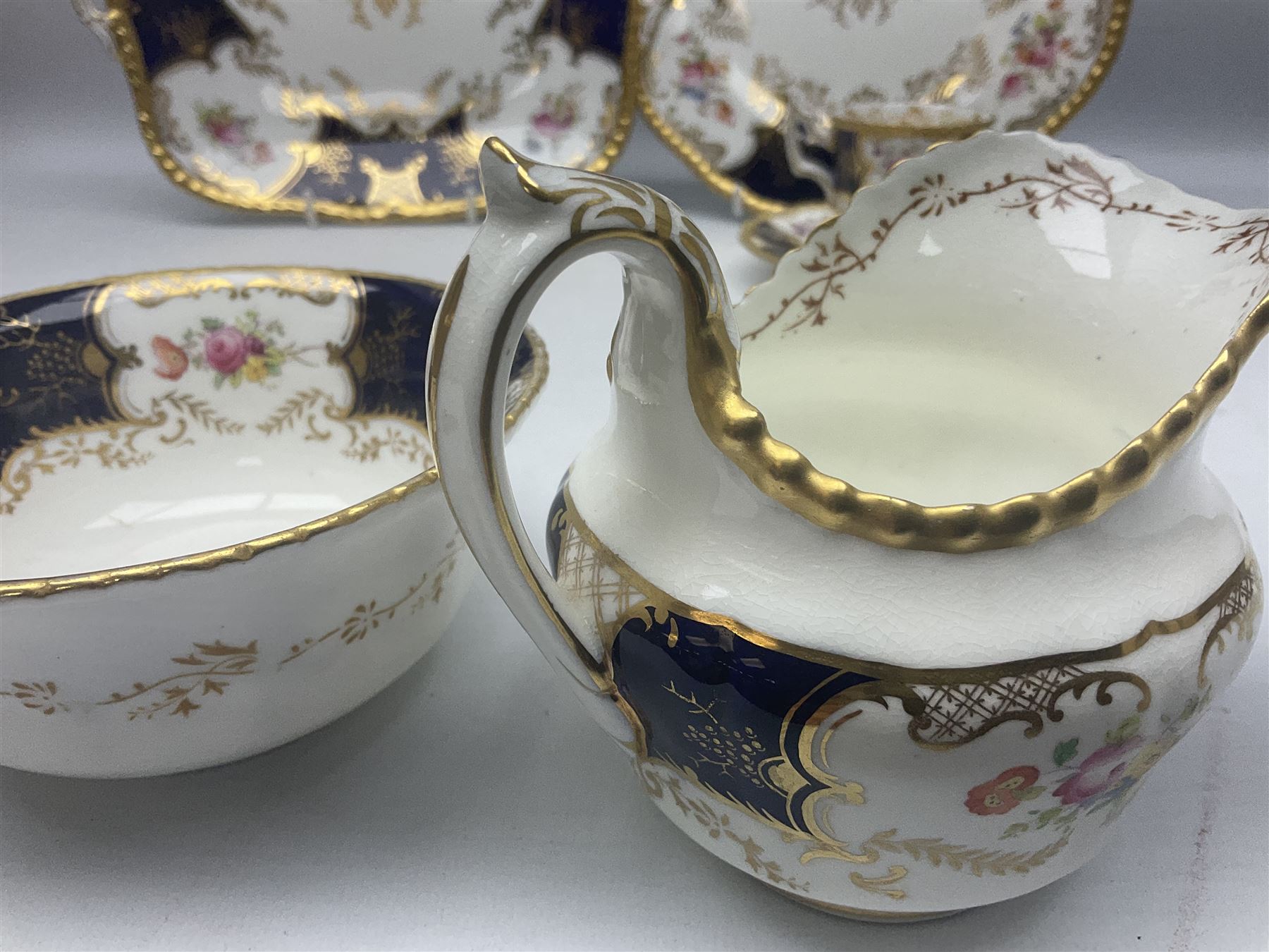 Coalport cobalt blue batwing pattern tea wares, decorated with finely enamelled floral sprays within gilt reserves, comprising teacup trio, coffee can and saucer and other cup and saucer, twin handled cake plate, milk jug and open sucrier, and circular plate retailed by T. Goode & Co London, pattern no Y2665,  all with green Coalport AD 1750 marks beneath, largest W26cm (11)