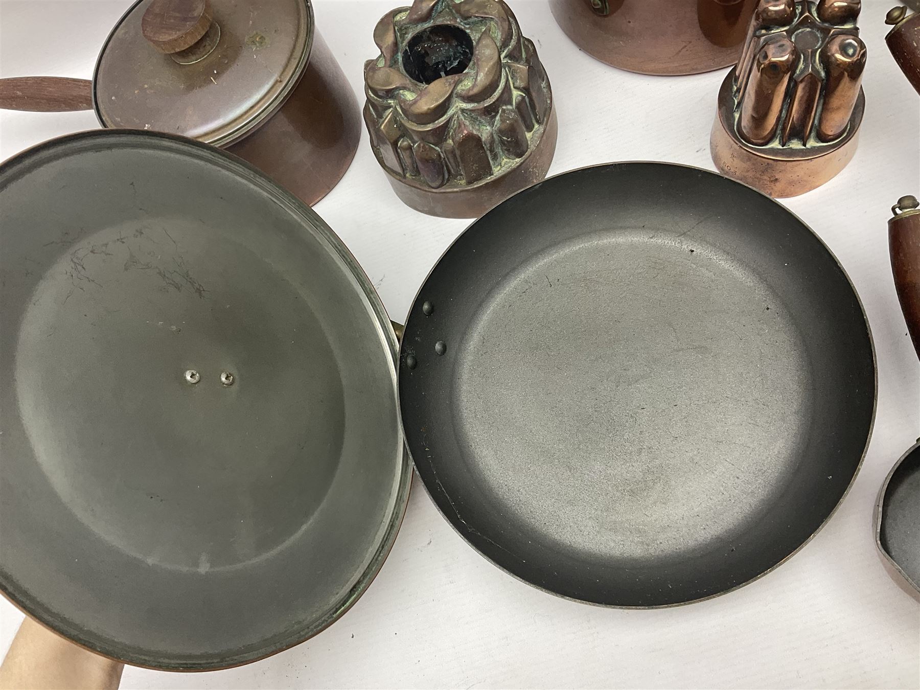Four Victorian copper moulds, together with a graduating set of copper pans with wooden handles and finials to covers, largest pan 