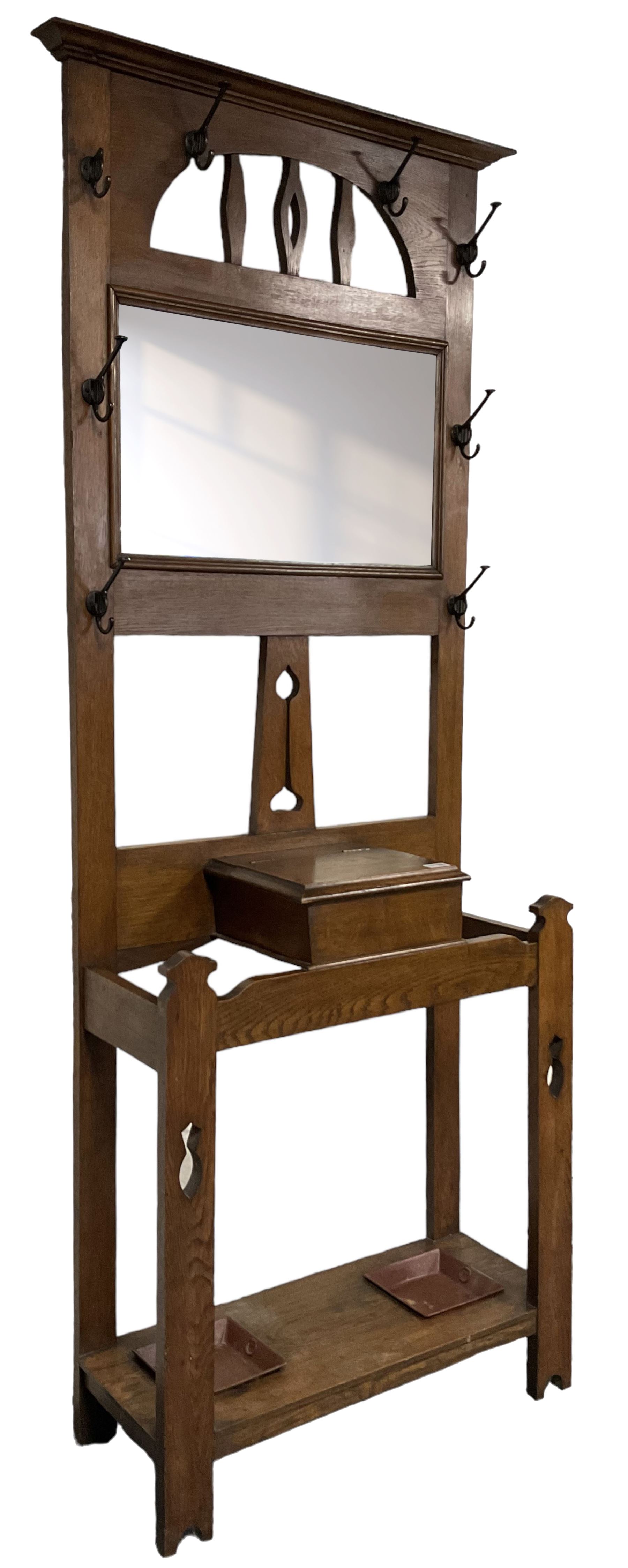 Arts & Crafts period oak hall stand, projecting moulded cornice over arched cut-out decorated with shaped vertical rails, fitted with rectangular bevelled mirror back over hinged glove compartment, on straight pierced supports with shaped pediments 