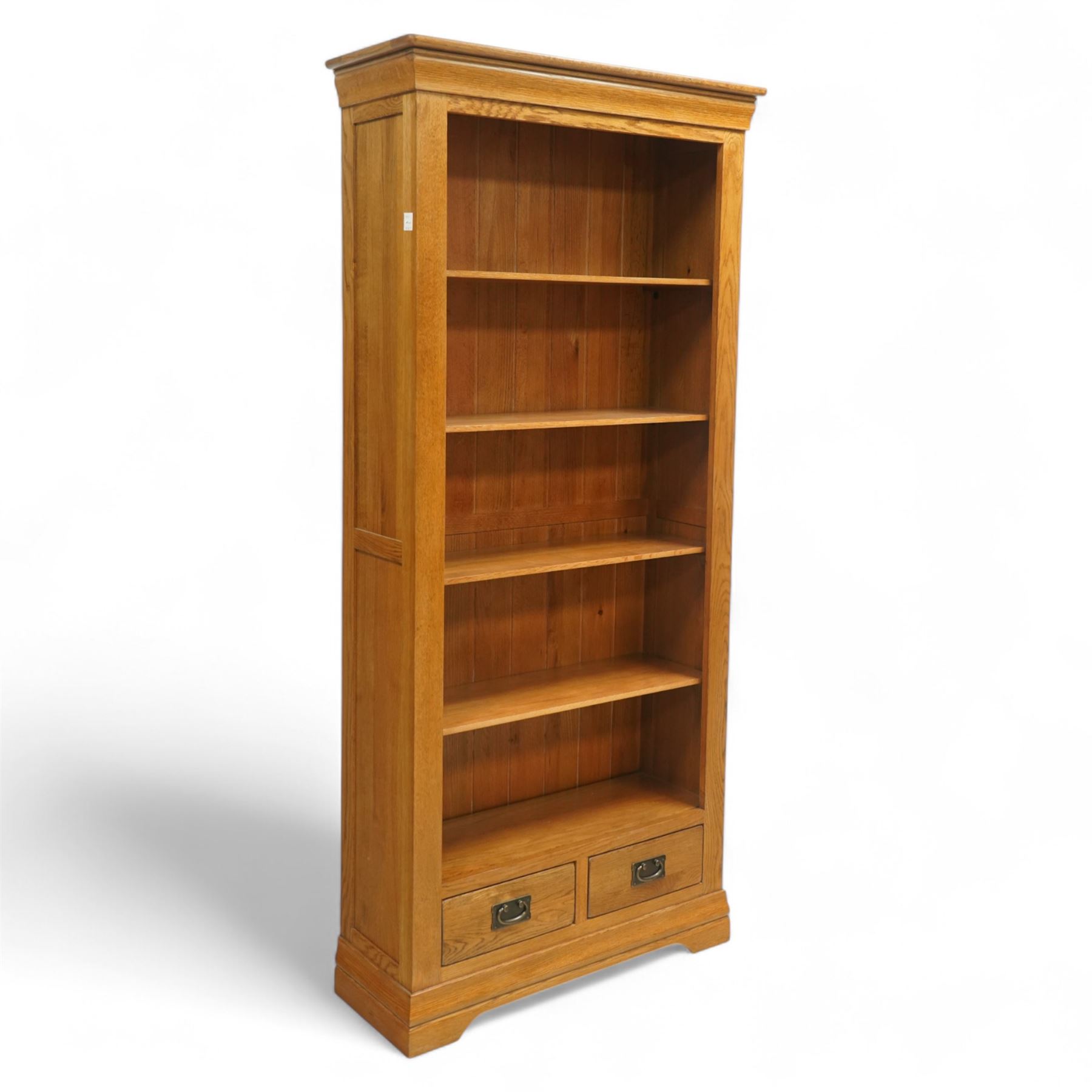 Contemporary oak bookcase, with moulded cornice above open shelved interior, fitted with four adjustable shelves and two short drawers with inset brass handles, panelled sides, plinth base
