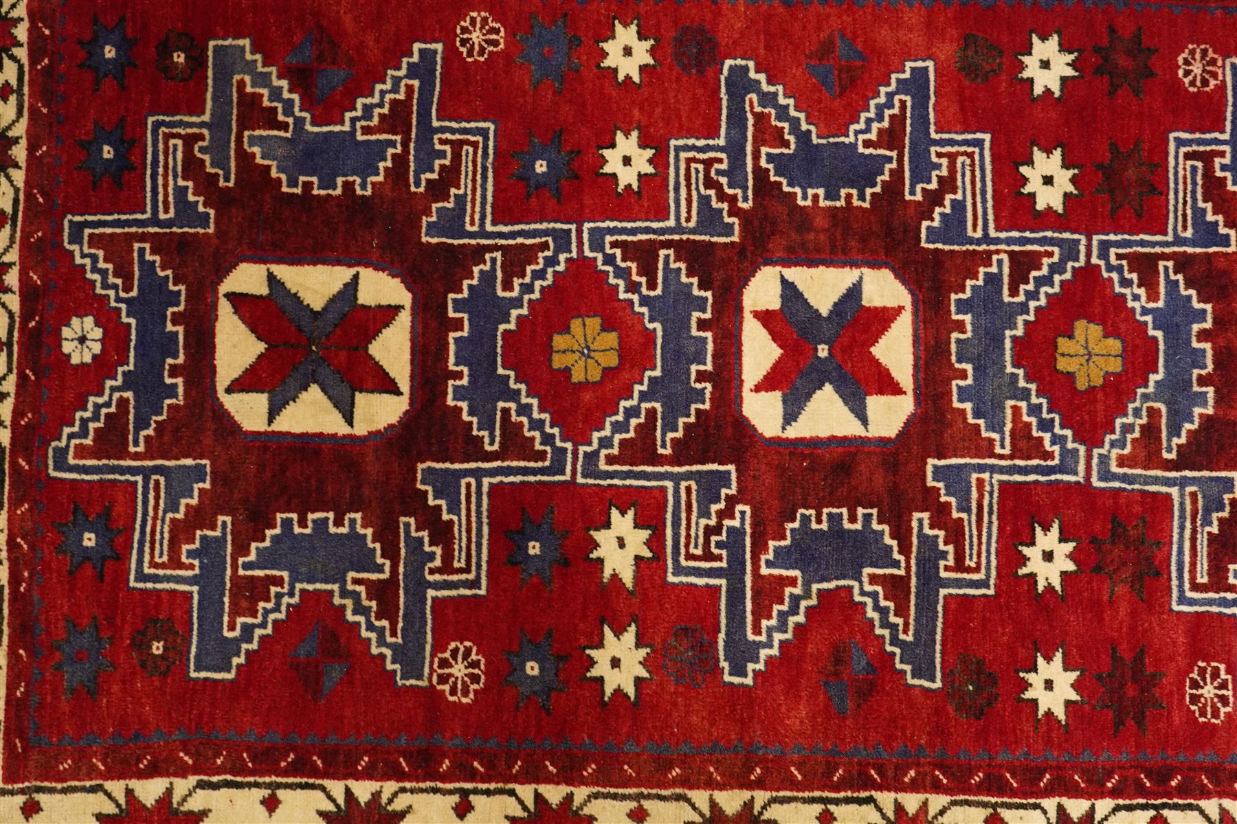 Caucasian Kazak hand-knotted rug, madder red ground with three large stepped geometric medallions in dark blue, ivory and red, surrounded by stylised star and flowerhead motifs, enclosed by ivory border with repeating eight-pointed stars, fringed ends