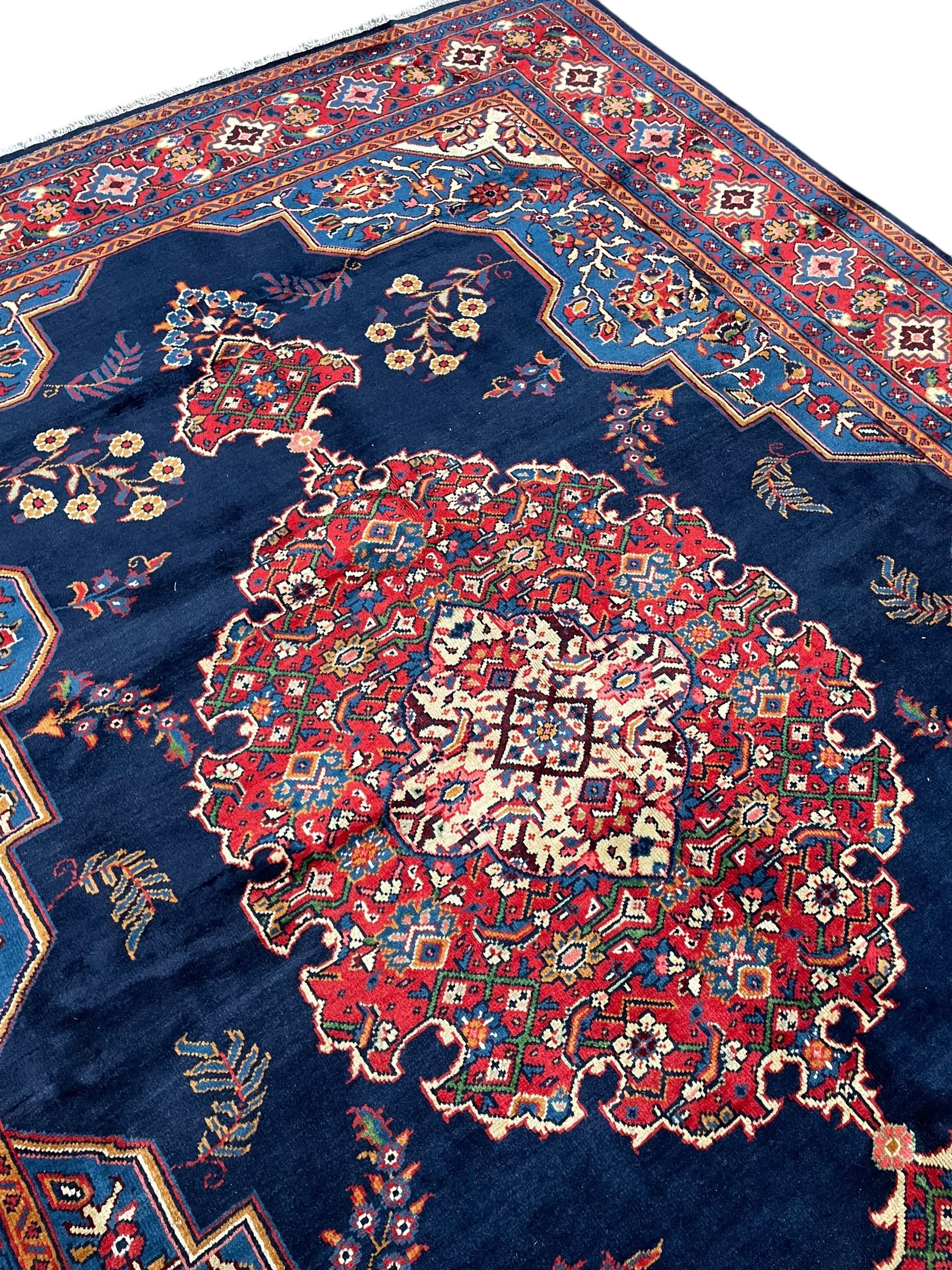 Persian Veis indigo ground carpet, the field with large pole medallion decorated with Herati motifs and surrounded by floral sprays, crimson ground border with repeating cross motifs and stylised flower heads, within guard stripes 