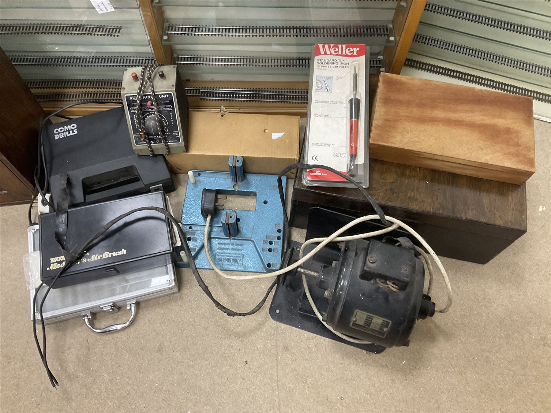 Six shelved cabinets for displaying ‘00’ gauge locomotives comprising plain plywood and white painted examples with track applied to various shelves, largest H63cm, W107cm, D27cm; Collection of tools for building model locomotives to include Weller PU-2D Soldering Pencil and Standard Tip Soldering Iron 20W/230V, Humbrol Modellers Airbrush, Power Supply Units and two wooden chests one of which housing a collection of tools including tweezers, scalping tools, wrenches etc 