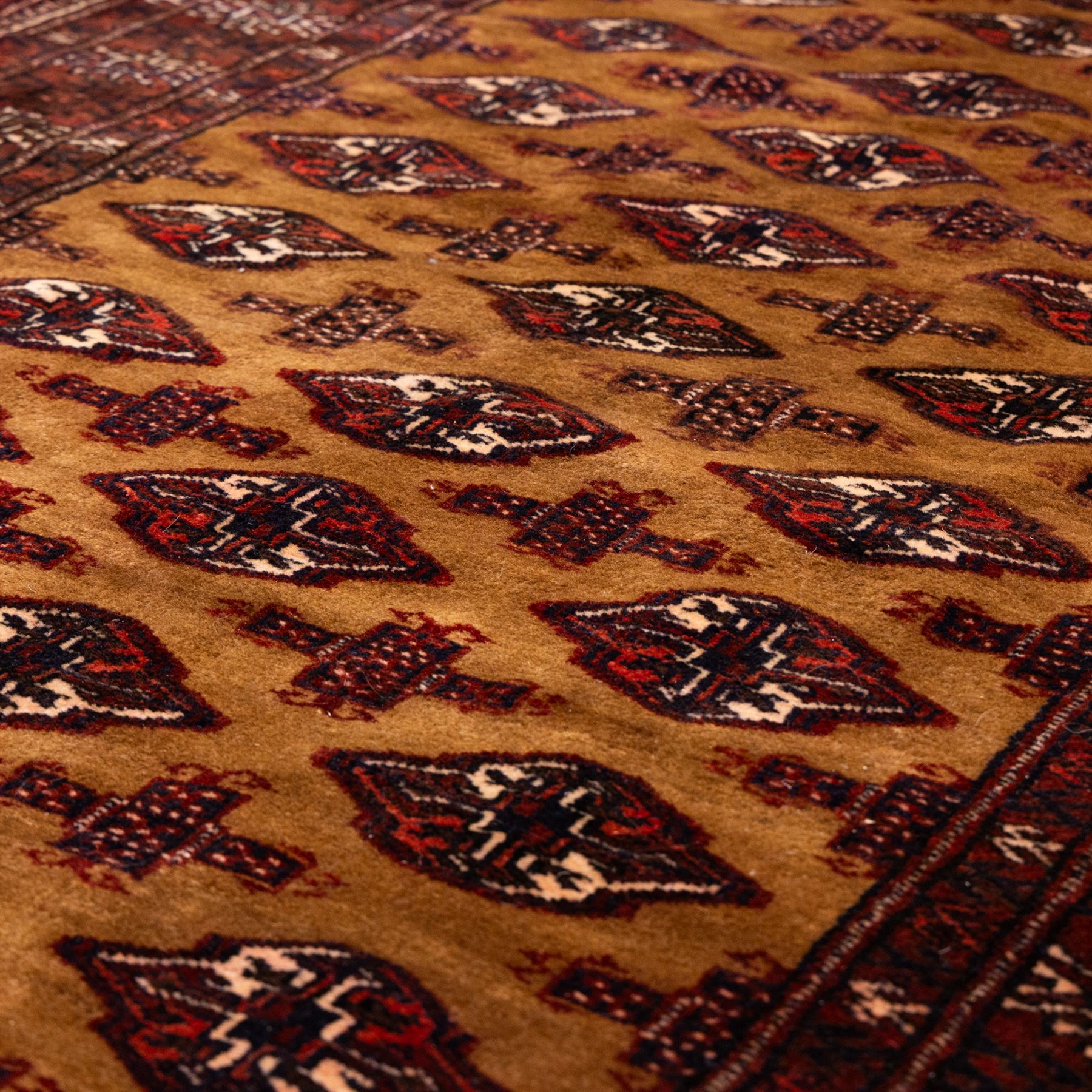 North East Persian Turkoman hand-knotted rug, camel brown field decorated with repeating rows of octagonal guls, interspersed with small geometric motifs enclosed within narrow guard borders in a palette of madder red, brown, and ivory, with cotton fringe ends  