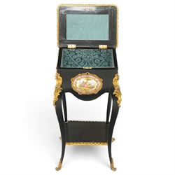 Early 20th century French ebonised sewing or work table, rectangular hinged top with foliate moulded gilt metal edge, enclosing upholstered interior, over a central Sevres style porcelain plaque depicting a courting scene, raised on cabriole supports with gilt metal carotuche and acanthus knee mounts, united by undertier with brass gallery terminating to gilt metal scroll feet