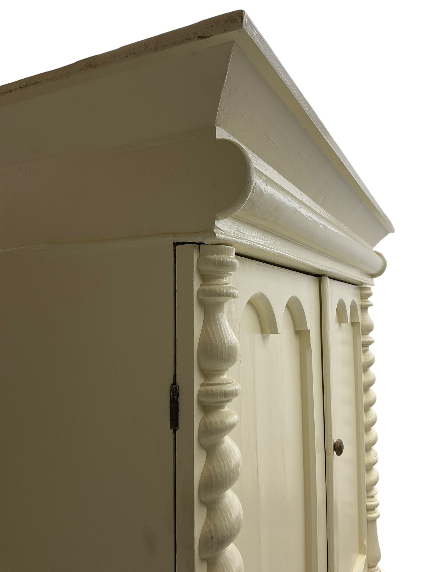 Victorian cream painted pine cupboard-on-chest or housekeeper's cupboard, projecting cornice over two double-arch panelled cupboard doors enclosing two shelves, flanked by spiral turned uprights, base fitted with two short over two long drawers, on bun feet