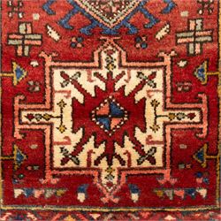 North west Persian Heriz runner, madder red field with a single column of alternating hooked and stepped lozenge medallions in ivory, blue, and terracotta, scattered with small cruciform and geometric motifs within a brick red border, angular motifs between narrow guard stripes 
