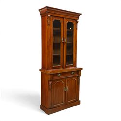 Victorian mahogany bookcase on cupboard of slender proportions, projecting cornice over dentil-frieze, fitted with twin-glazed doors enclosing three shelves, flanked by acanthus corbels, the base fitted with single frieze drawer over panelled cupboard, on skirted base