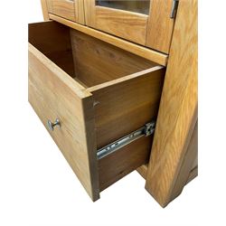 Light oak bookcase display cabinet, projecting square cornice over glazed double doors enclosing three adjustable shelves, single drawer base, on stile supports