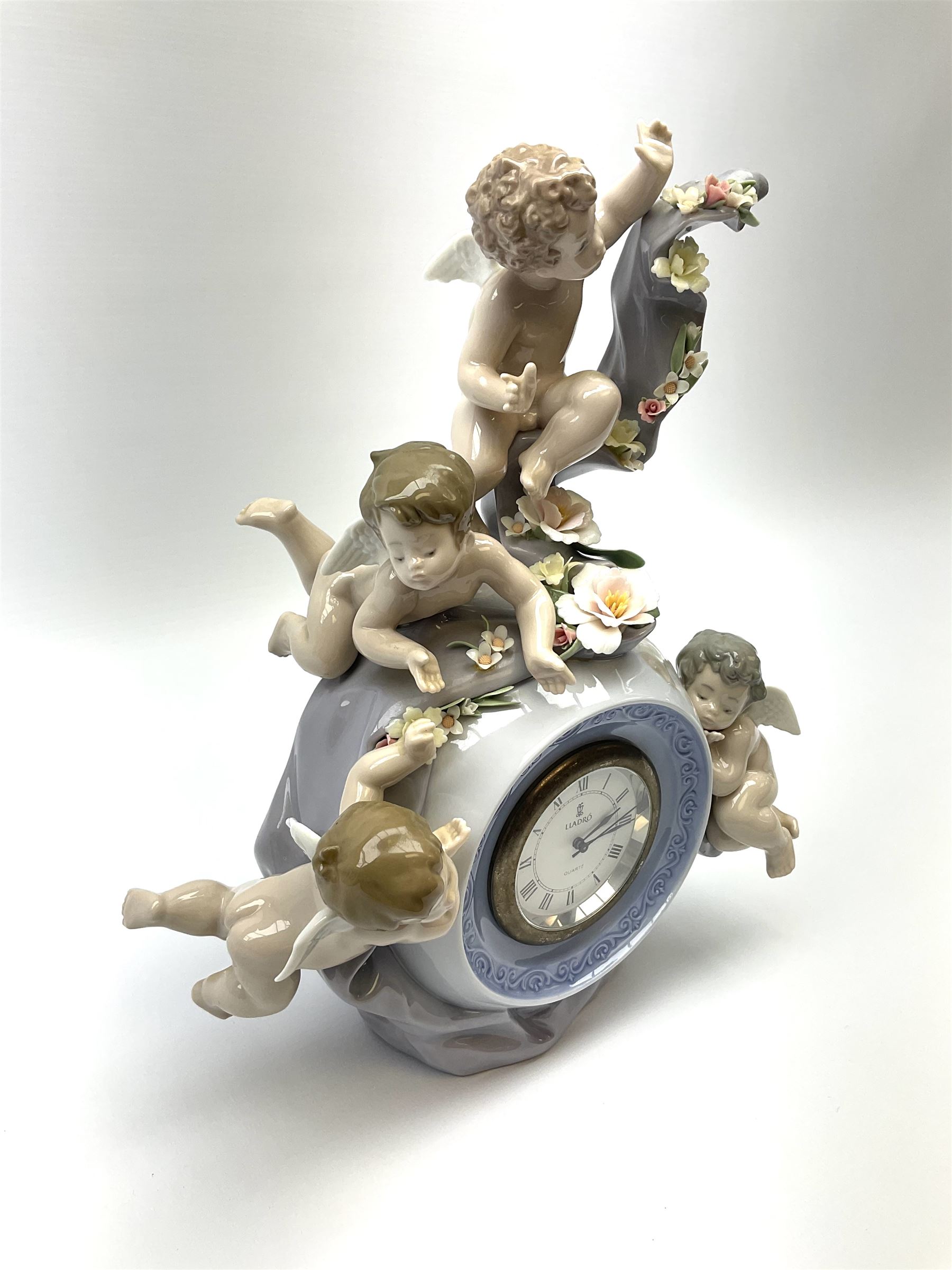 A Lladro mantel clock modelled as a globe with inset clock, surmounted by four putti and floral garlands, with blue printed mark and impressed 5973 beneath, H29cm.