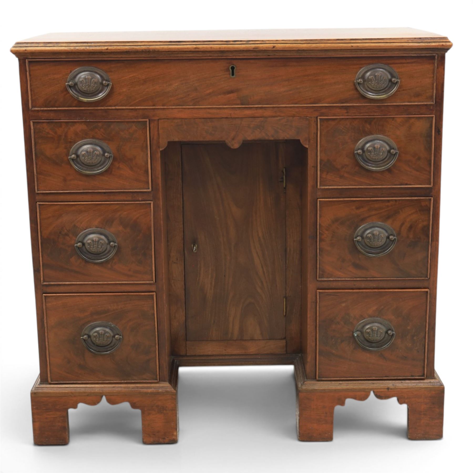 Early 20th century Georgian design figured walnut kneehole desk, rectangular moulded top over one long frieze drawer, kneehole recess with cupboard and drawer above, flanked by six short drawers with oval pressed brass handle plates, moulded plinth base on bracket feet