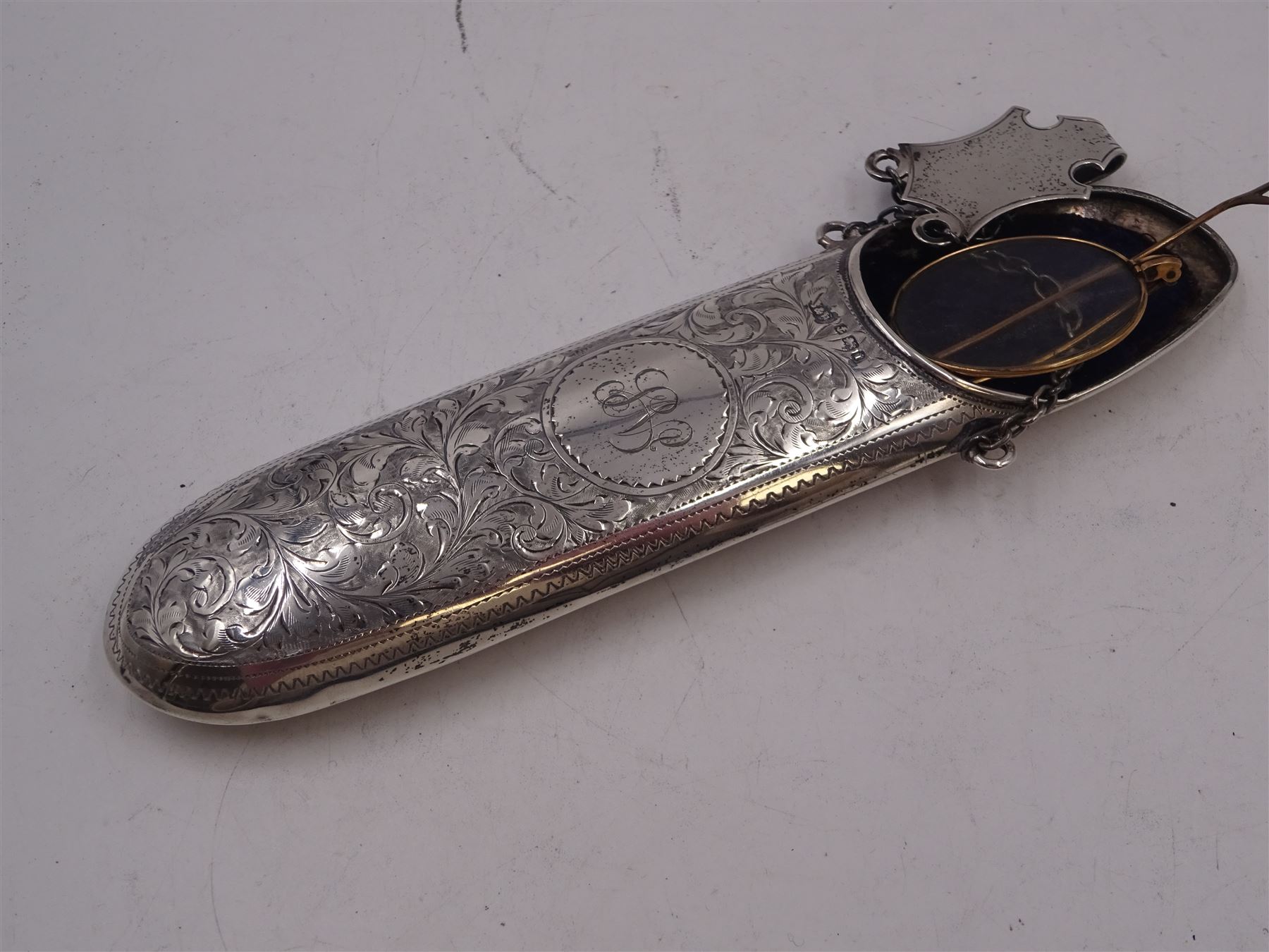 Victorian silver hip flask, of oval form, with engraved foliate and scroll decoration, and monogrammed shield shaped cartouche to centre, with plain collar and cap, H11cm, hallmarked Chester 1899, maker's mark worn and indistinct, together with an Edwardian silver glasses case, of oval form, with engraved foliate and scroll decoration, and monogrammed circular shaped cartouche to centre, with opening to top, revealing velvet lined interior, with silver shield clip, H17.5cm hallmarked to case and clip Sanders & Hill,  Birmingham 1908, with a pair of gold plated glasses 