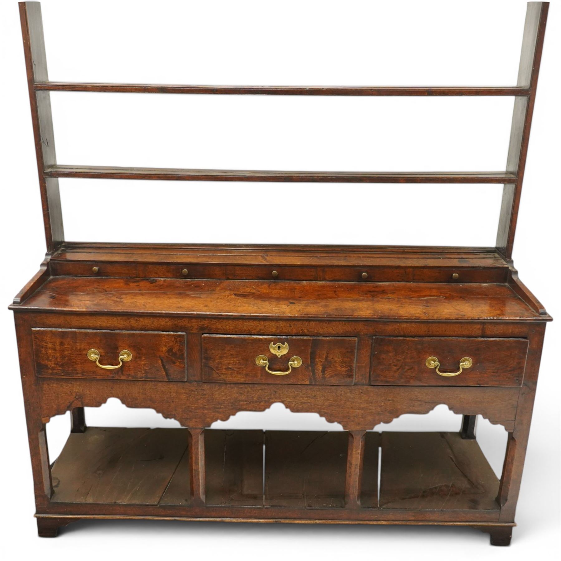 18th century Georgian oak dresser base with plate rack, the three-tier plate rack with shaped frieze, the base with rectangular top with raised back fitted with five spice drawers, over three drawers with brass swan neck handles, raised on six square chamfered supports united by undertier 