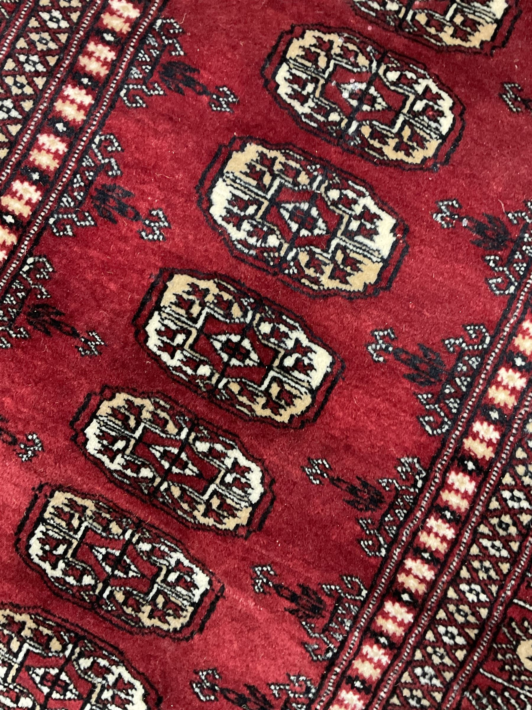 Persian Bokhara rug, red ground and decorated with single row of Gul motifs, multiple band border with geometric design